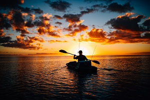 man paddling fishing kayak at dusk