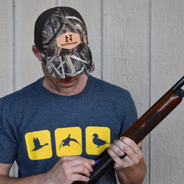 man holding gun wearing mossy oak blades leather patch hat