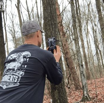 man mounting a trail camera to a tree