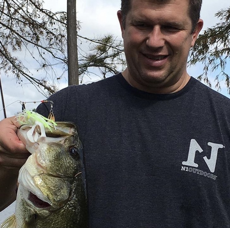 man holding largemouth bass wearing N1 Outdoors fishing shirt