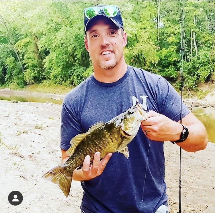 man holding smallmouth bass and wearing N1 Outdoors fishing shirt