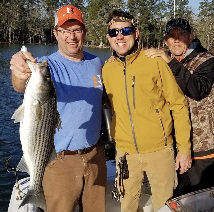 Maston and Andy holding striped bass wearing N1 Outdoors fishing shirt and hat