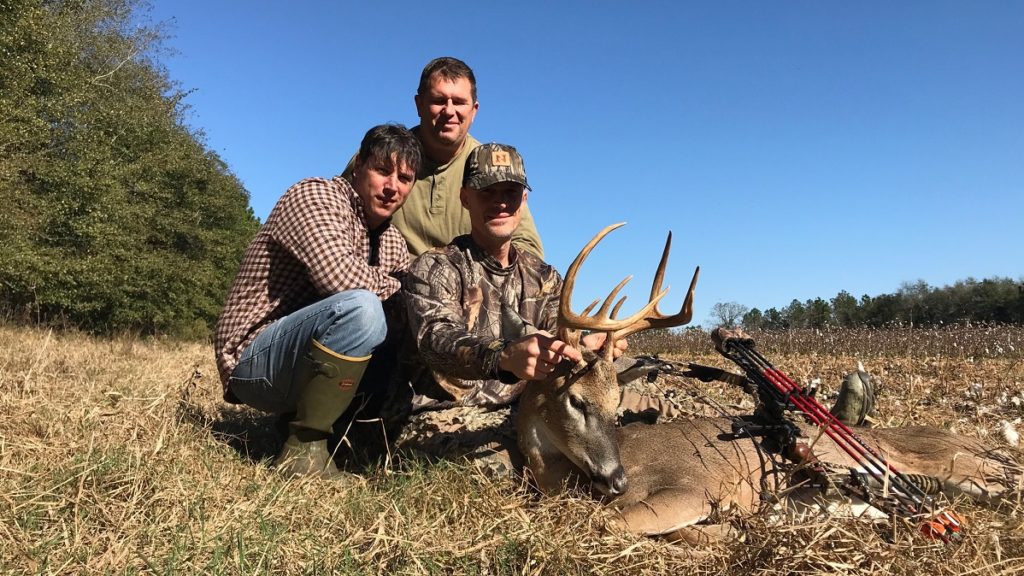 three men posing with whitetail archery buck in cotton field