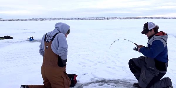 man holding bent ice fishing rod catching fish