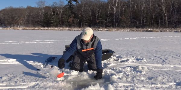 man scooping ice slush out of ice fishing hole