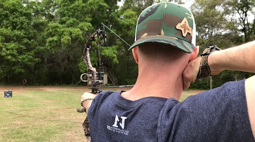 man shooting compound bow at target