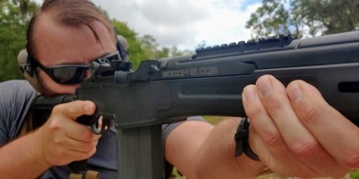 man looking down rifle barrel with open sight