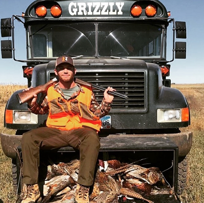 man sitting in front of bus with pheasants he killed hunting