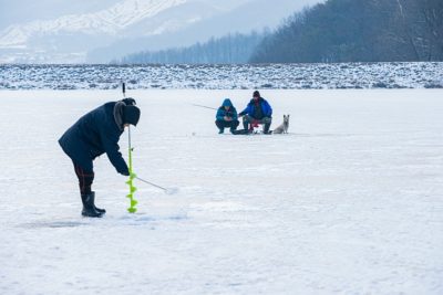 man drilling hole for ice fishing
