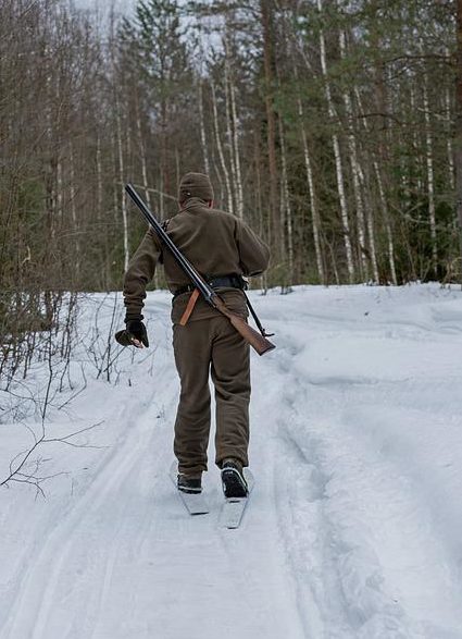 man skiing in snow with hunting gun