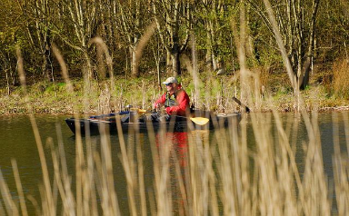 man fishing from kayak behind reeds
