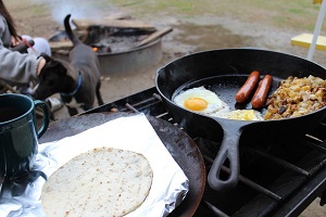 sausage and eggs cooking over campfire
