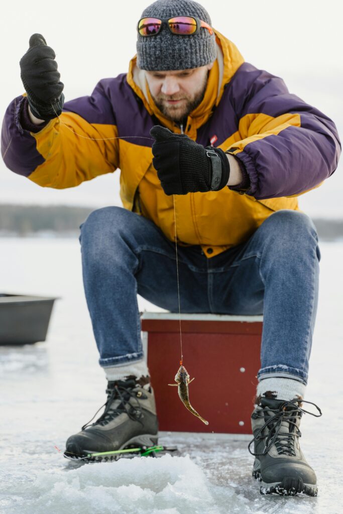man ice fishing pulling out small fish