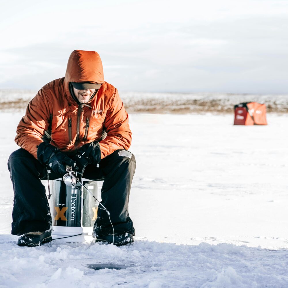man ice fishing with tent in background