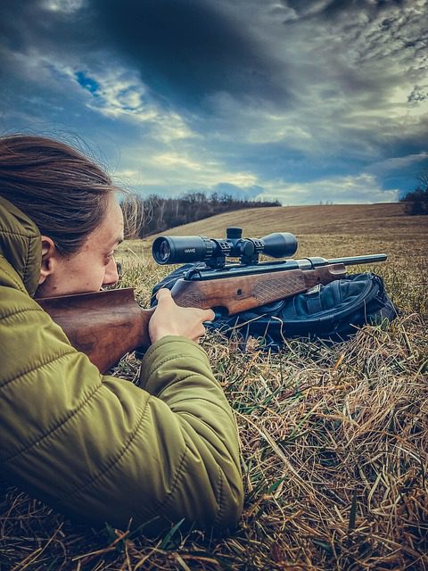 woman looking through rifle scope in field