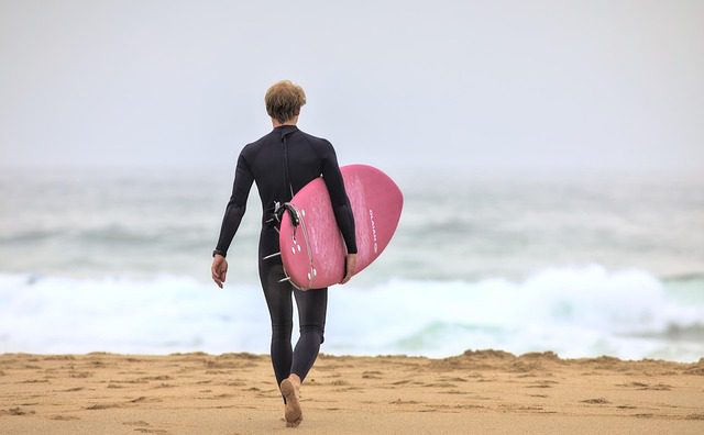 man in wetsuit holding surfboard