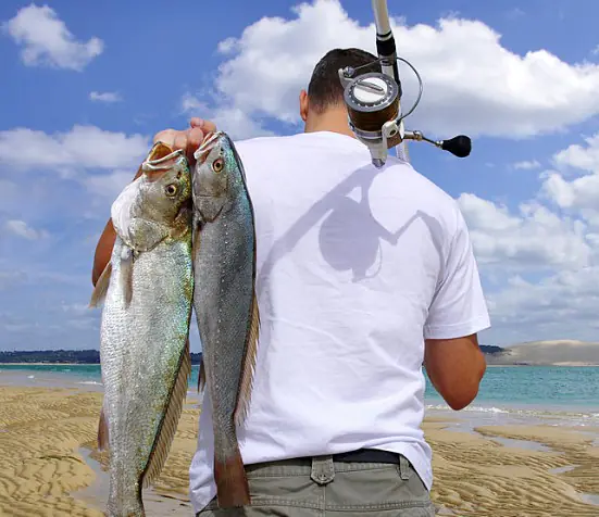 man holding 2 fish over shoulder and fishing rod