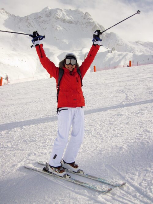 woman in red ski jacket holdking ski poles in air